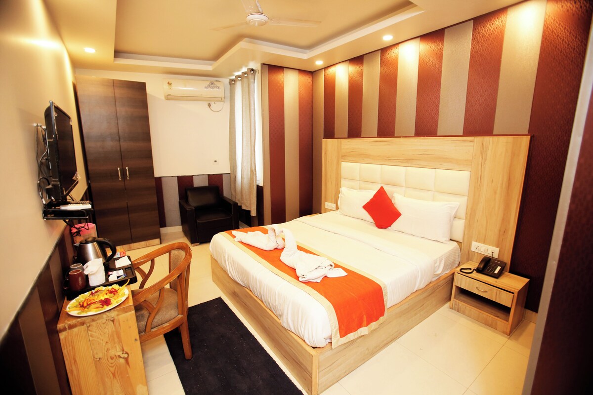 A hotel room with a bed, a wooden nightstand, a desk with a chair, and a television.