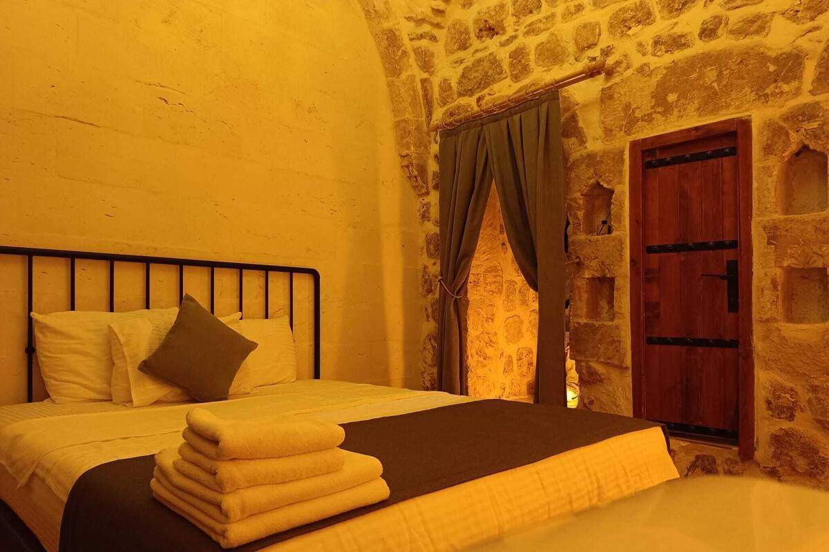A bed with a metal frame, white and brown pillows, and a stack of yellow towels.