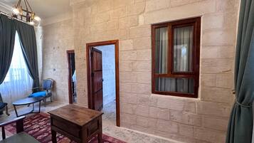 A room with a stone wall, a wooden table, a blue chair, and a window with curtains.