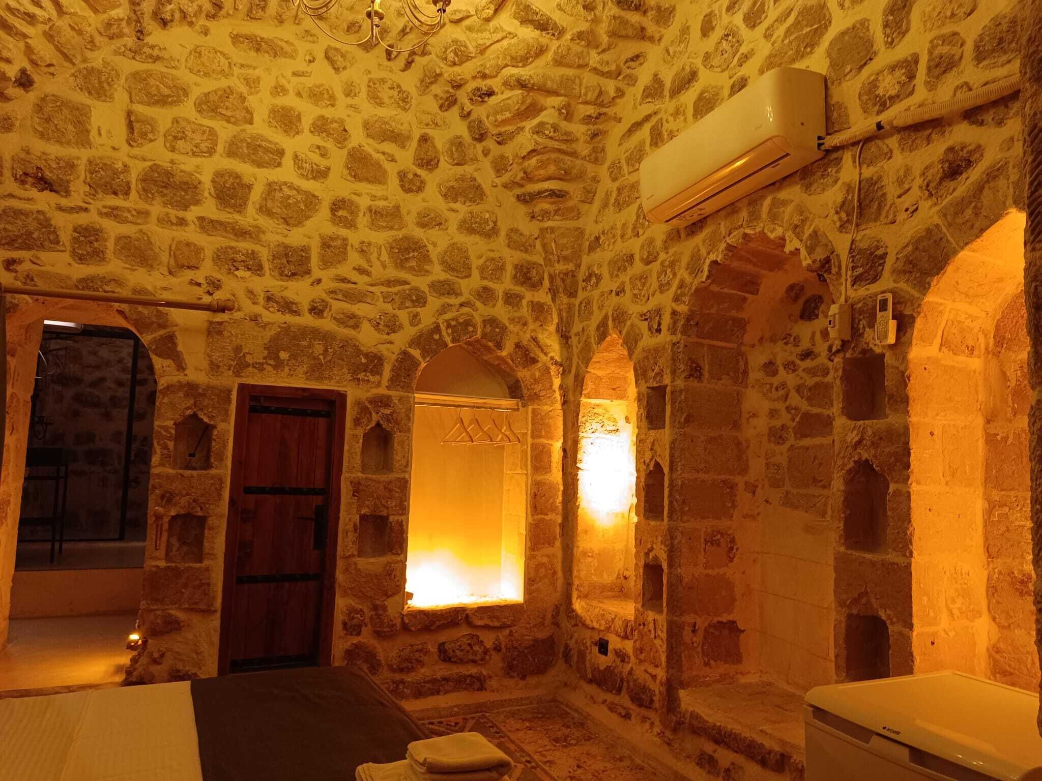 A stone-walled room with a bed, a wooden door, and a wall-mounted air conditioner.