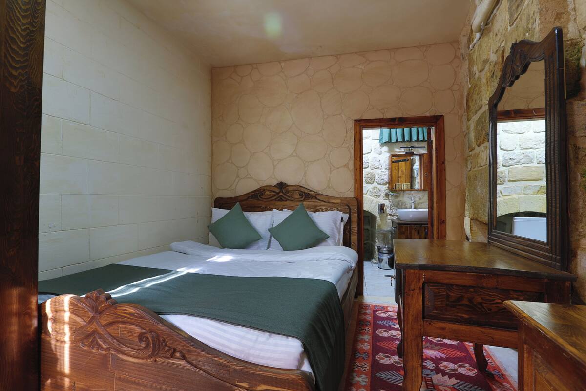 A bedroom with a wooden bed, a nightstand, a mirror, and a stone wall.