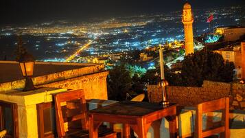 A night view of a cityscape with a prominent tower and a table with chairs in the foreground.
