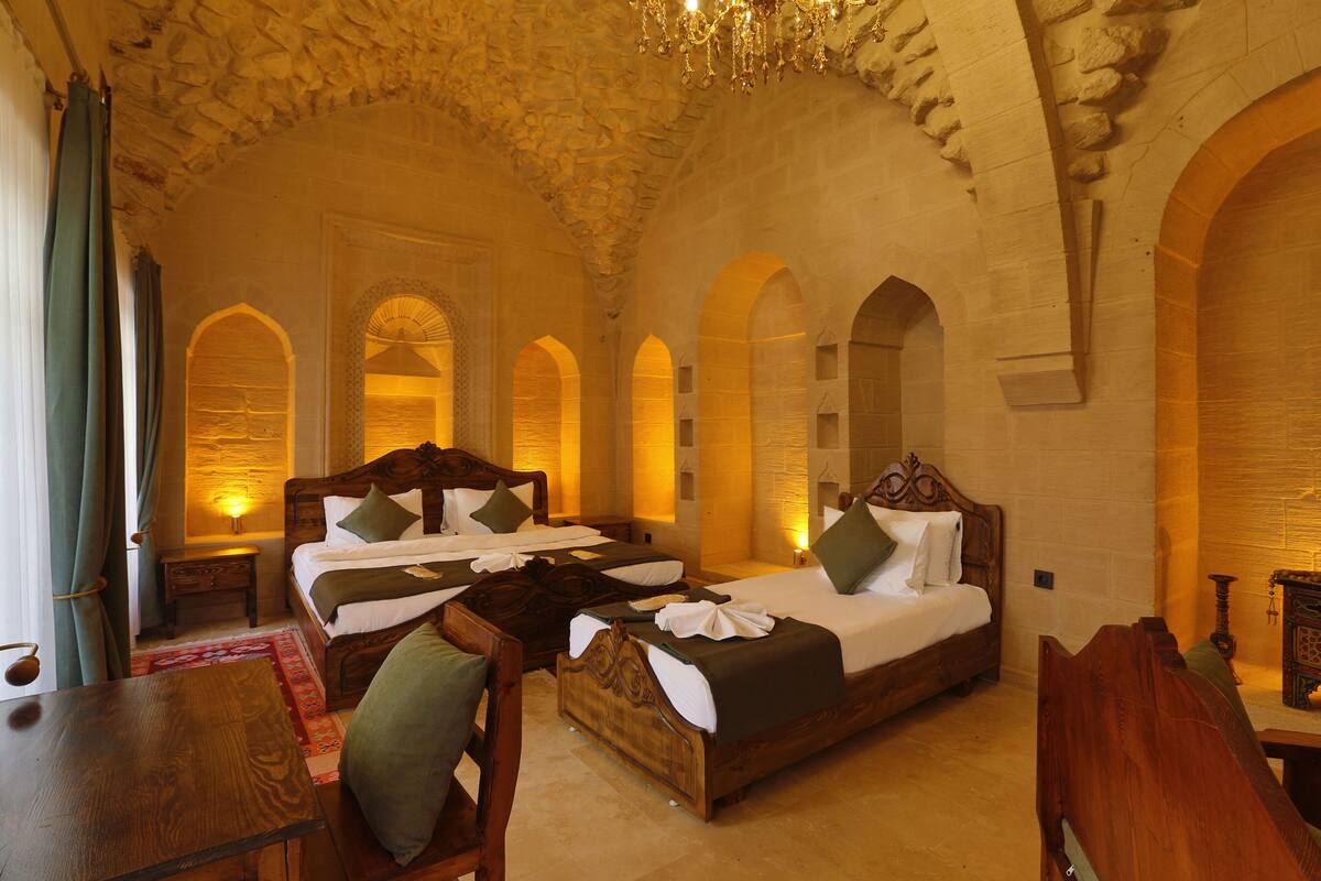 A spacious room with three wooden beds, a chandelier, and stone arches.