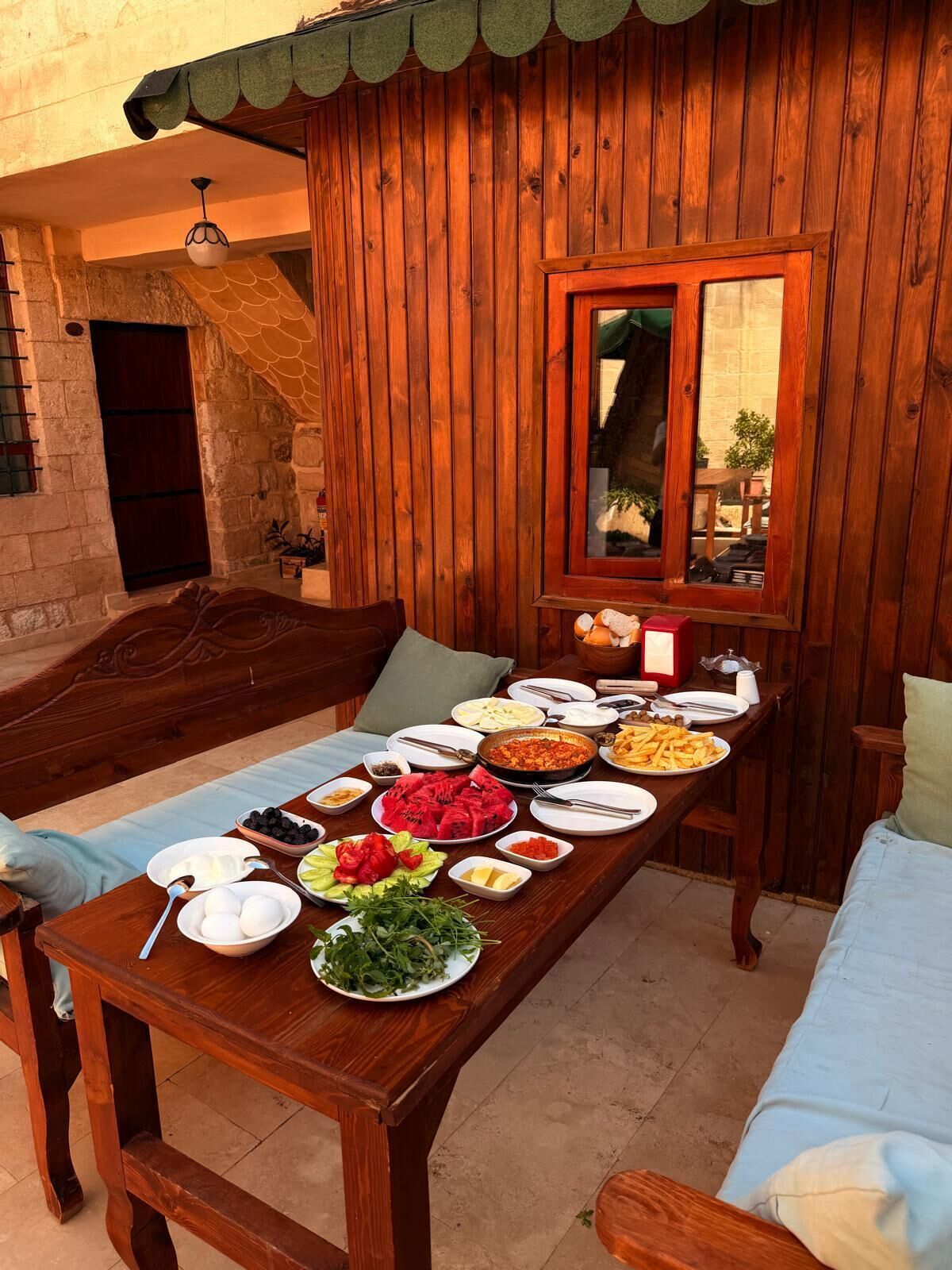 Una mesa de madera dispuesta con varios platos, una pared de piedra y un banco de madera.
