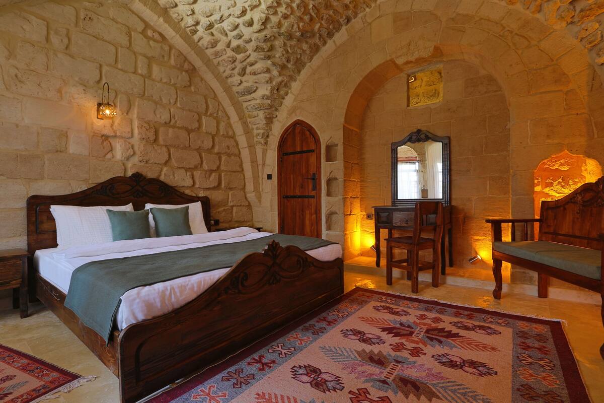 A stone-walled bedroom with a wooden bed, a desk, and a chair.