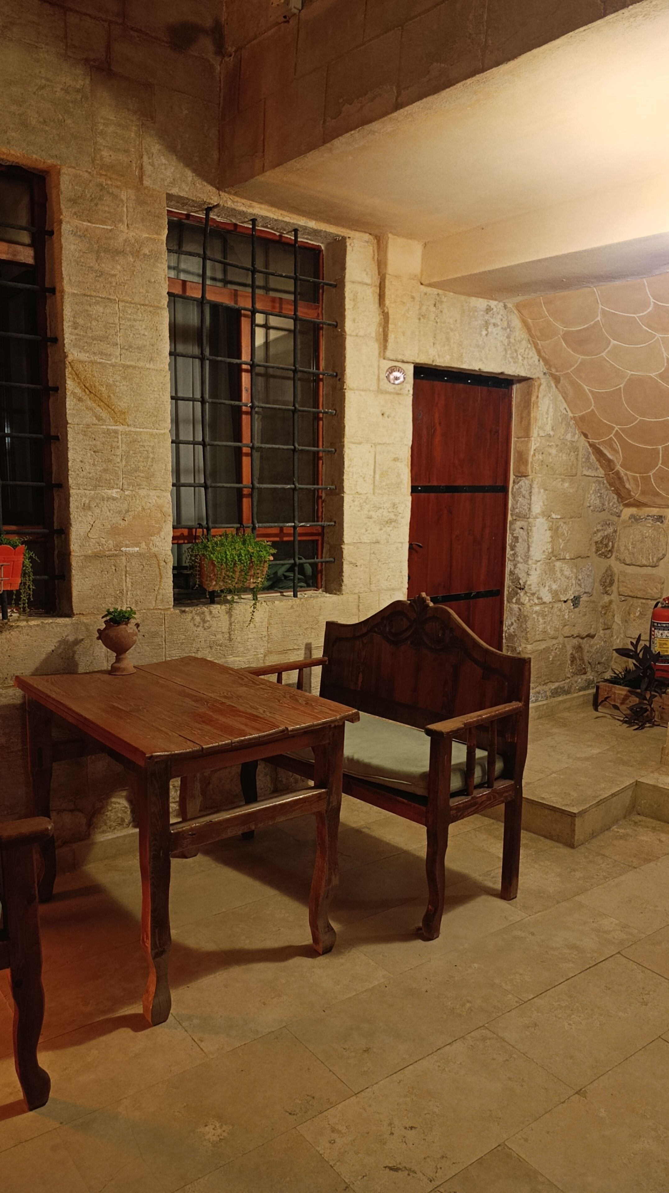 Un intérieur rustique en pierre, avec une table et une chaise en bois, une fenêtre à barreaux et un escalier en pierre.