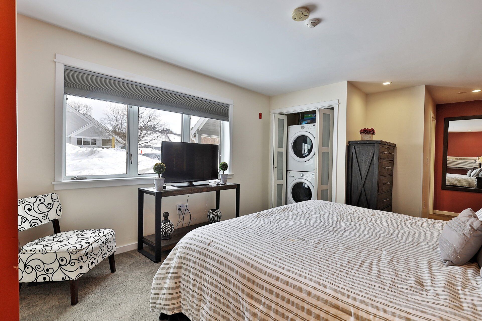 A bedroom with a bed, a TV, a washing machine, a dresser, and a chair.
