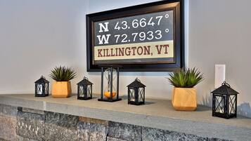 A framed sign with coordinates and location, flanked by potted plants and lanterns on a stone ledge.