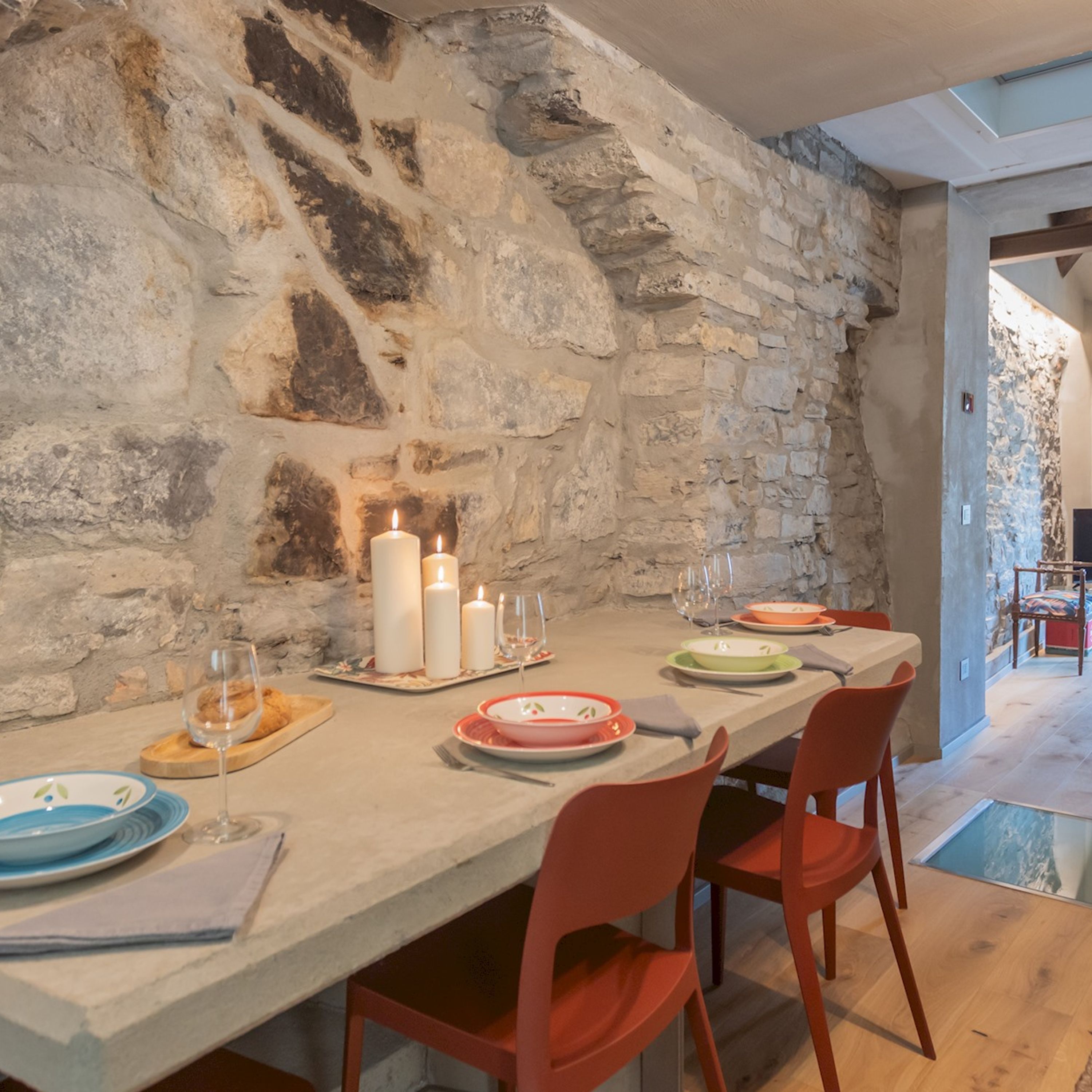 Un muro de piedra con una mesa de comedor para cuatro personas, con platos, vasos y velas.