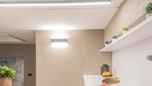 Een moderne keuken met een wit aanrecht, een ingebouwd spoelbak en een spatwand. Er staan potplanten op het aanrecht en hangt een lamp boven de spoelbak.
