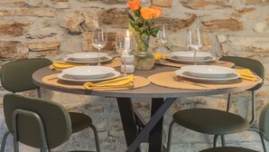 Een ronde eettafel voor vier personen, gedekt met borden, bestek en een vaas met bloemen.