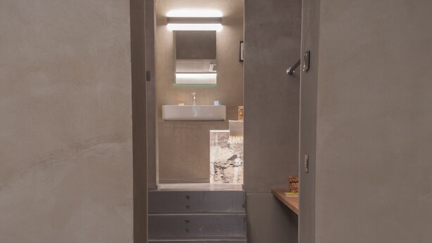 Een moderne badkamer met een douchecabine van glas, een wastafel en een spiegel. Er staat een houten bankje met een dienblad waarop twee muffins en twee kaarsen staan.