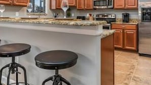 A kitchen with wooden cabinets, a central island with stools, a microwave, and a refrigerator. - CG 9025 Shadow Mountain Epic Villa By Disney Theater Game Room Pool Spa (Davenport)