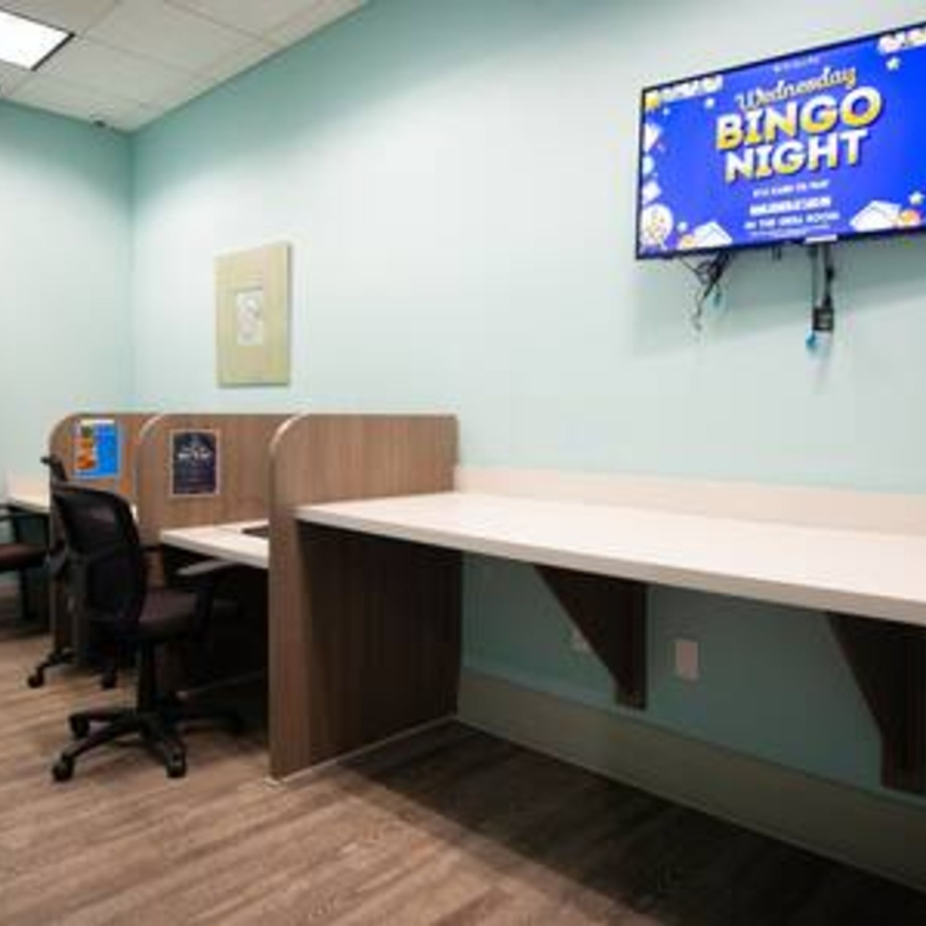 A room with a long table, wooden partitions, and a television displaying a 'Wednesday Bingo Night' sign.