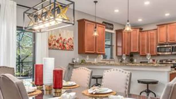 A dining area with a glass table, chairs, and a chandelier. There are wooden cabinets and a kitchen in the background. - CG 9025 Shadow Mountain Epic Villa By Disney Theater Game Room Pool Spa (Davenport)