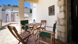 An outdoor patio with a wooden table and chairs, stone walls, and a stone staircase. - Kyriaki's Traditional House (Chania)