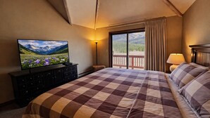 Een hotelkamer met een groot bed, een televisie op een dressoir, een balkon met gordijnen en uitzicht op de bergen.