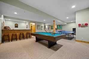 Une table de billard avec des tabourets, une table de ping-pong et un coin bar avec des tabourets.