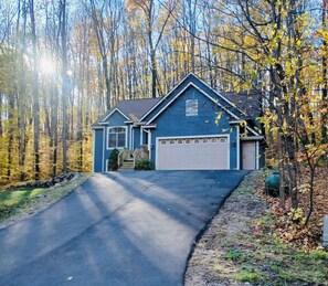 Une maison d’habitation avec un garage, entourée d’arbres et dotée d’une allée.