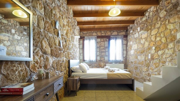A bedroom with stone walls, a wooden bed, a nightstand, and a mirror.