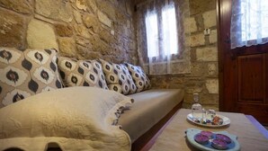 A stone-walled room with a bed, a table with a plate of snacks and candles, and a window with curtains.