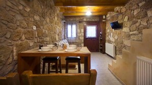 A rustic stone-walled dining area with a wooden table set for four, a wooden bench, and a television mounted on the wall.