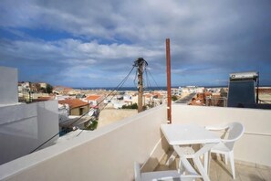 Eine Dachterrasse mit Tisch und Stühlen, mit Blick auf eine Stadtlandschaft aus Gebäuden und einem klaren Himmel.