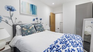 A neatly arranged bedroom with a bed, pillows, a nightstand, a lamp, a wardrobe, and a mirror. - Little Venice Maisonette (London)
