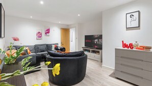 A modern living room with a black sofa, a black bean bag chair, a TV, a bookshelf, and a dresser. - Little Venice Maisonette (London)
