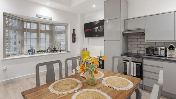 A modern kitchen with grey cabinets, a built-in microwave, and a large flat-screen TV mounted above the counter. - Little Venice Maisonette (London)