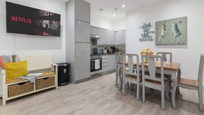 A modern kitchen with grey cabinets, a built-in oven, and a dining area with a wooden table and chairs. - Little Venice Maisonette (London)