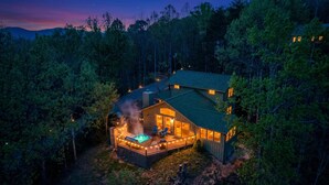 A lodge with a hot tub, a deck, and a large window overlooking a forested area. - Pet-Friendly · 3 Kings · Hot Tub · Arcade + Pool Table (Gatlinburg)