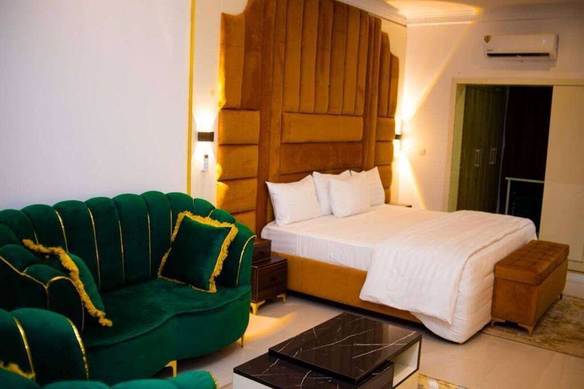 Un dormitorio con una cama grande, un sofá verde, un cabecero de madera y un pequeño banco de madera.