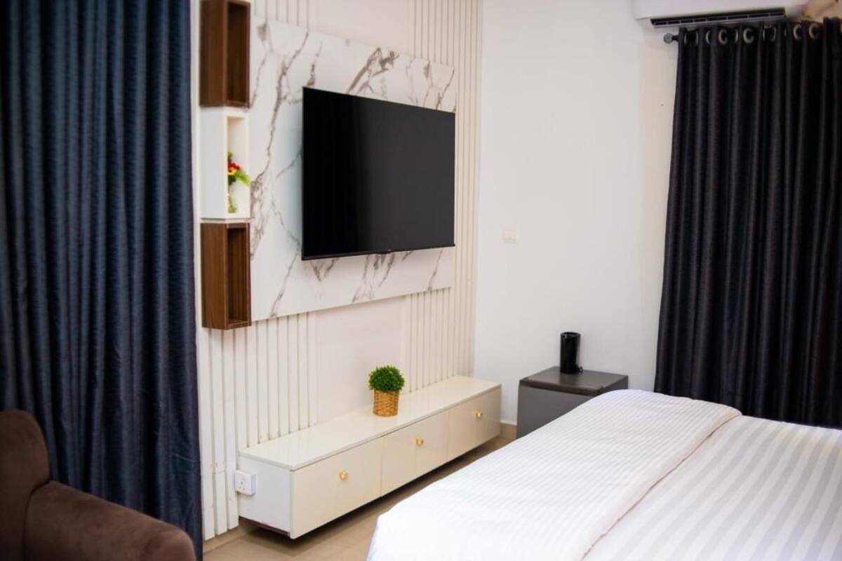 Un dormitorio moderno con una cama grande, un televisor fijado en una pared de mármol, una mesita de noche y una planta pequeña en el tocador.