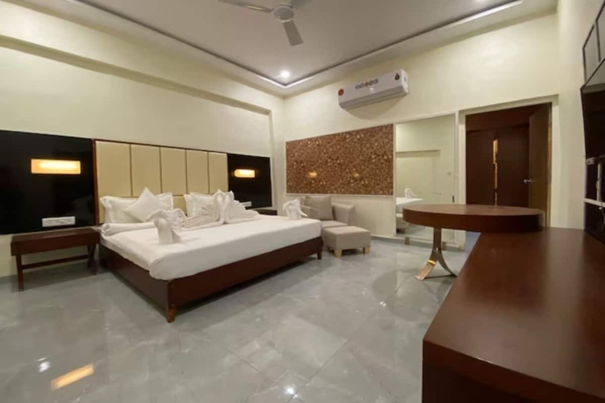 A modern hotel room with a large bed, a seating area, a small table, and a ceiling fan.