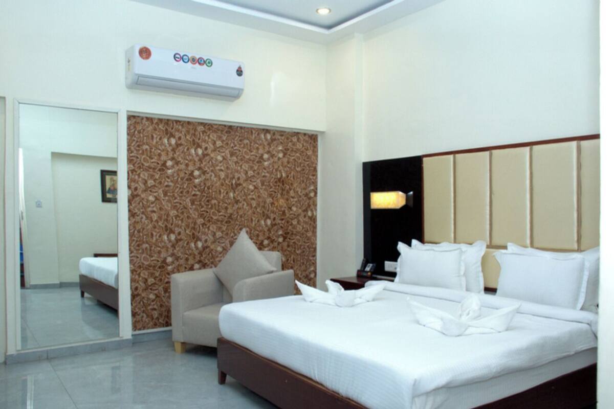 A modern hotel room with a large bed, a sofa, a wall-mounted air conditioner, and a mirror.