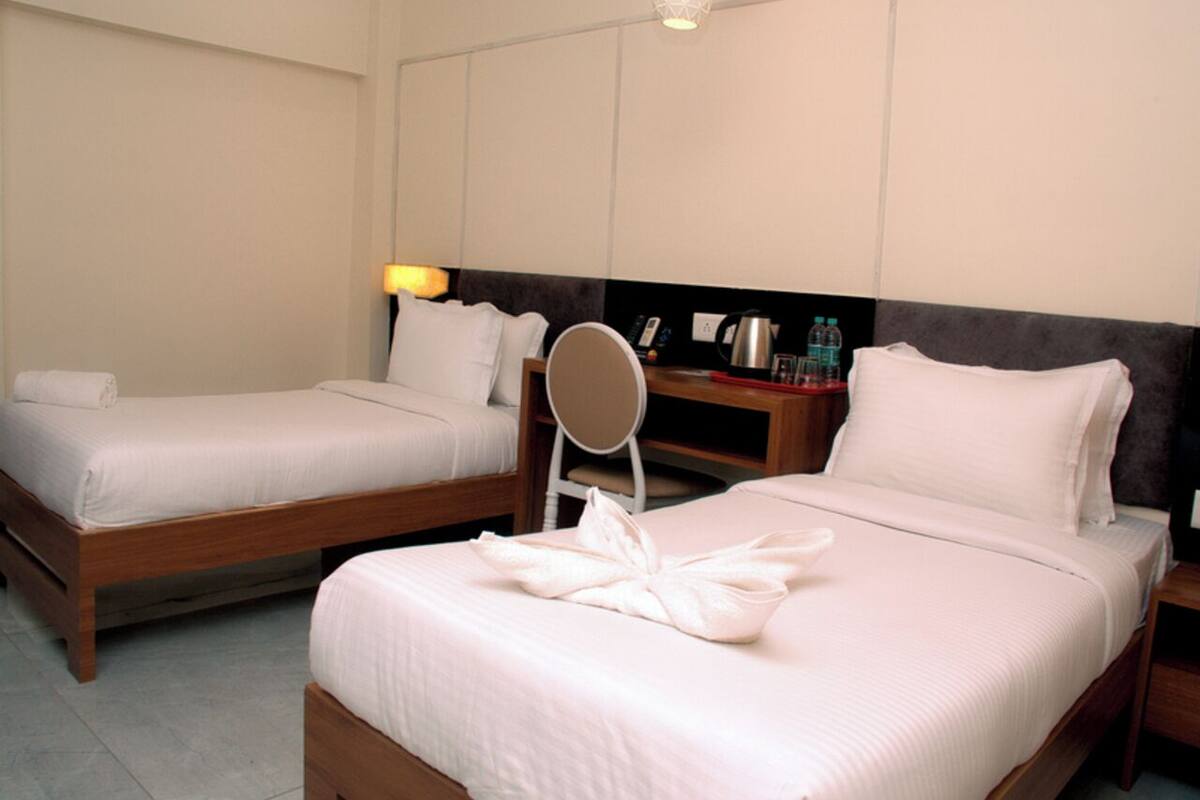 A hotel room with two beds, a bedside table with a lamp, a mirror, and a small table with toiletries.