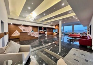 A spacious lobby with a reception desk, seating area, and large windows offering a view. -  Santu GSM an ECO Resort (Ghogha)