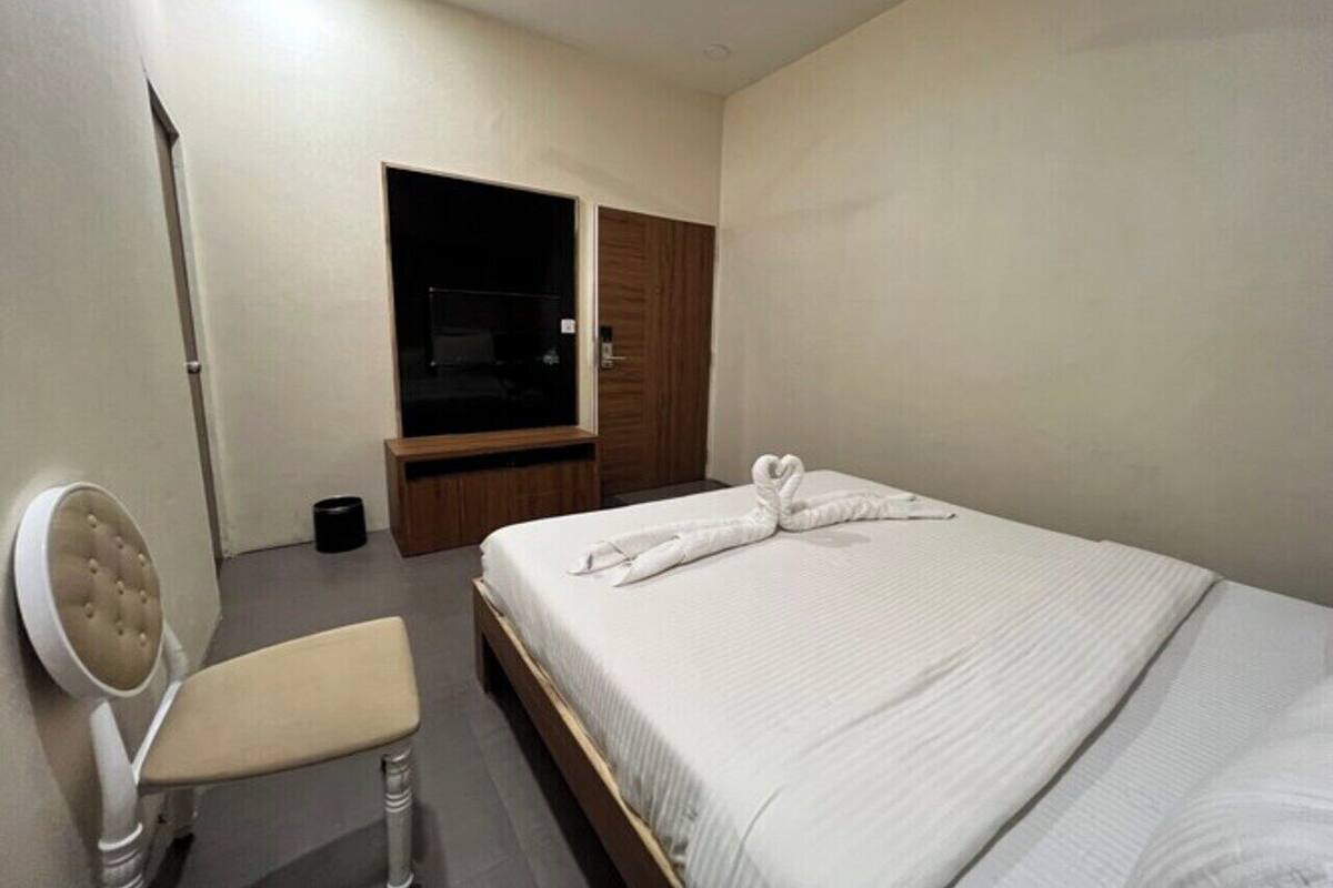 A hotel room with a bed, a chair, a TV, and a wardrobe.