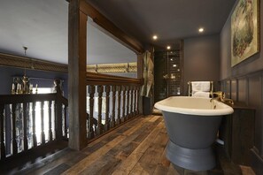A bathroom with a freestanding bathtub, wooden flooring, and a view through an open doorway.