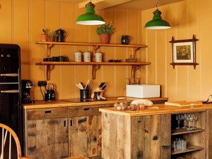 A kitchen with wooden cabinets, a coffee machine, and hanging green pendant lights.