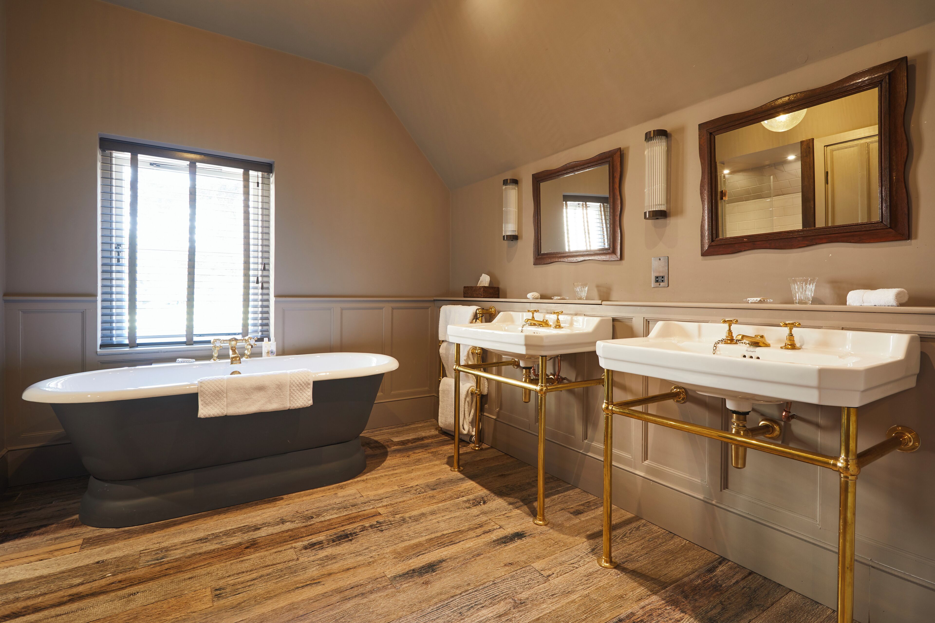 A bathroom with a freestanding bathtub, two sinks with gold fixtures, and a large mirror above the sinks.
