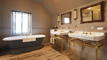 A bathroom with a freestanding bathtub, two sinks with gold fixtures, and a large mirror above the sinks.