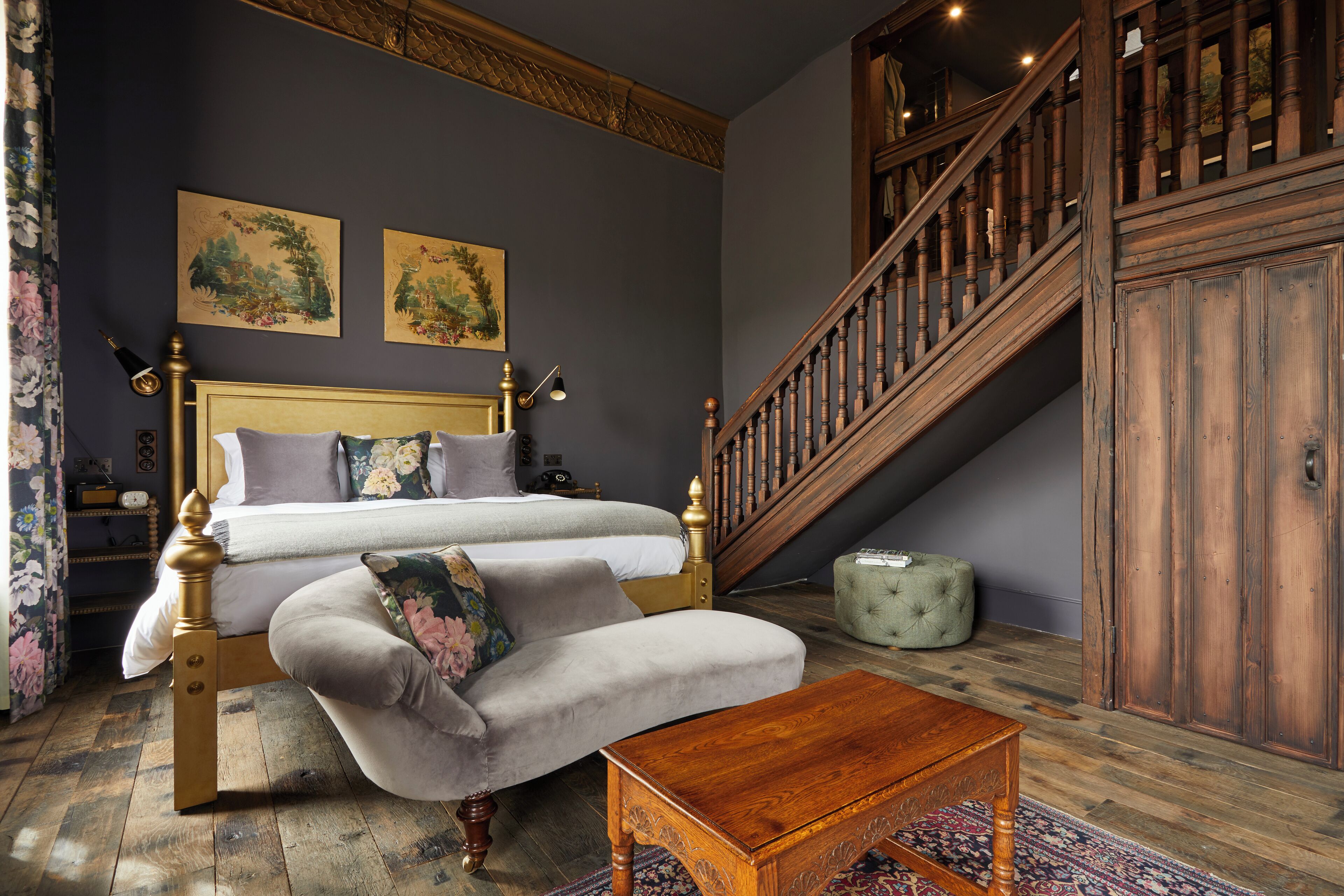 A bedroom with a large bed, a wooden staircase, and a green ottoman.