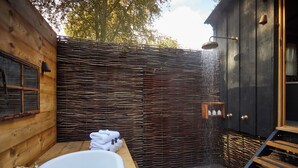 A wooden cabin bathroom with a large bathtub, a shower with a rain showerhead, and a wooden bench. - THE PIG at Bridge Place - Kent (Canterbury)