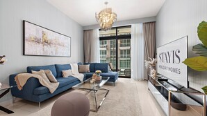 A modern living room with a blue sofa, a glass coffee table, and a large TV screen displaying 'STAYIS HOLIDAY HOMES'.