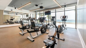 A modern gym with various exercise equipment, large windows, and a view of the outdoors.