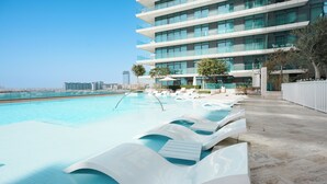 A modern hotel with a pool area featuring tiered, wavy white lounge chairs and a clear view of the city skyline.