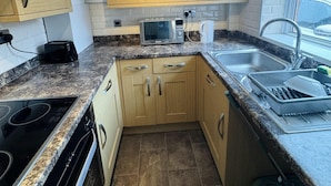 A modern kitchen with wooden cabinets, a granite countertop, a built-in microwave, and a stainless steel sink. - Entire 4-bed House in Sunderland (Sunderland)