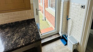 A kitchen with a granite countertop, a wooden cabinet, a sliding glass door leading outside, and a small trash bin. - Entire 4-bed House in Sunderland (Sunderland)